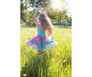 young girl dancing in field with hands above head