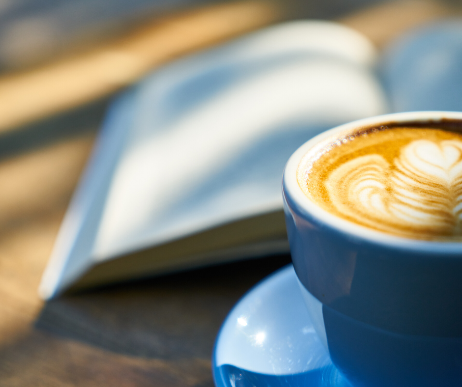 blue cup of decorated coffee and book on table - community